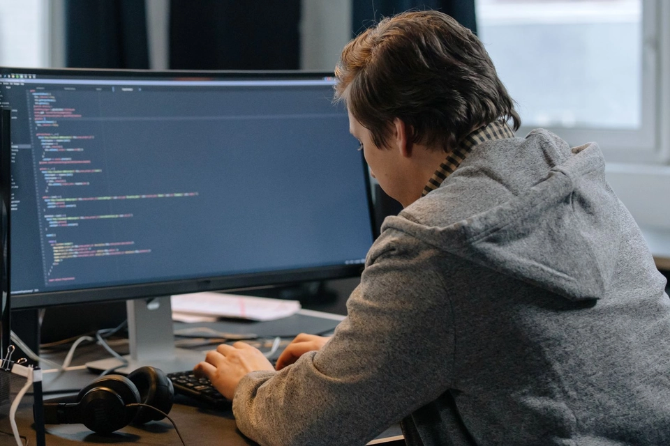 Programmeur in grijze hoodie typt aan zijn bureau